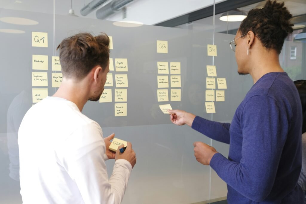 Two people collaborating in front of a glass wall covered in sticky notes organized by quarterly planning columns.
